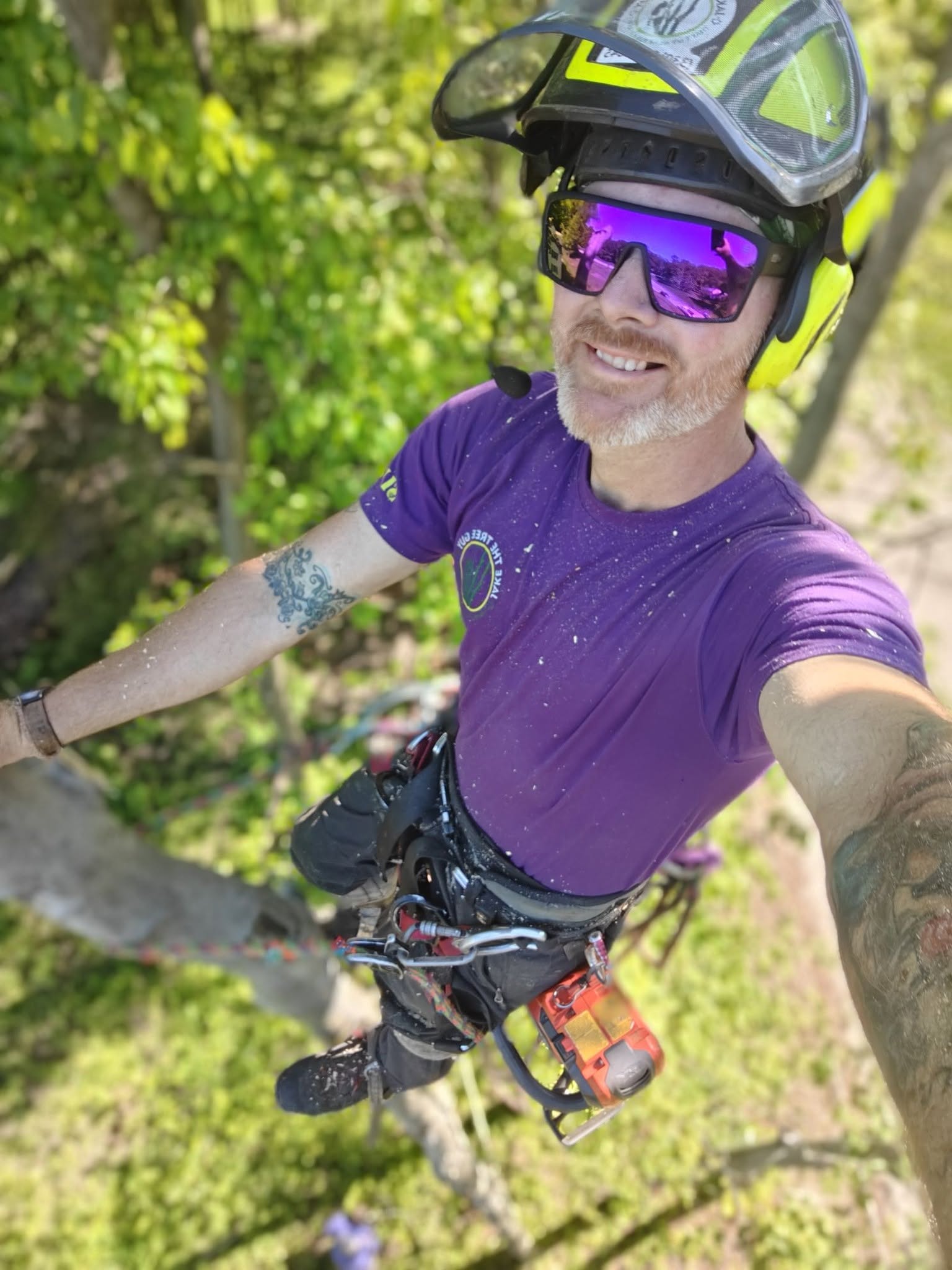 Jake smiling selfie in full climbing harness with chainsaw high in a tree